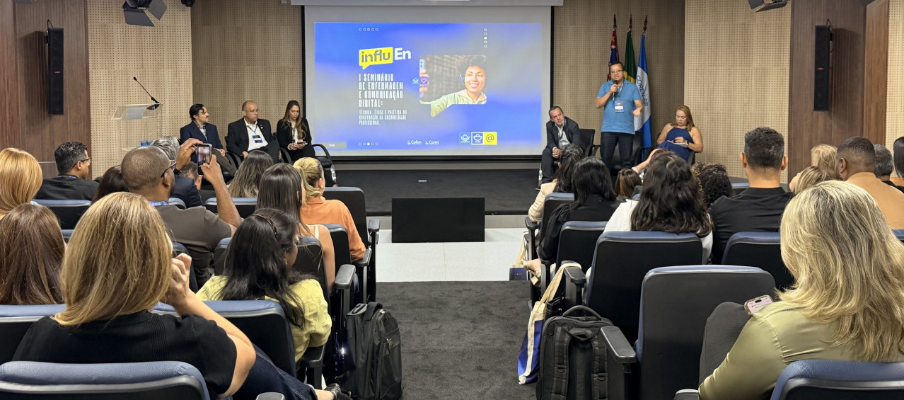 Uma pessoa falando ao microfone para muitas pessoas em um auditório