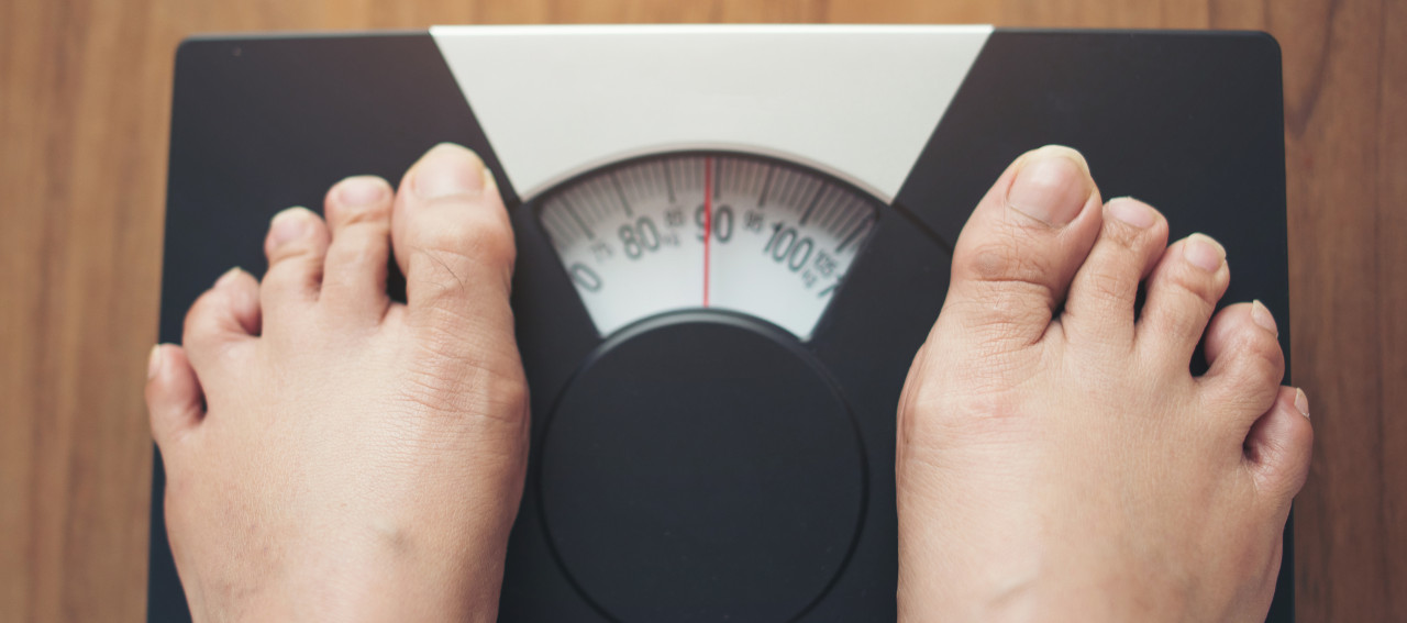 Woman feet standing on Weight Scale on wooden background