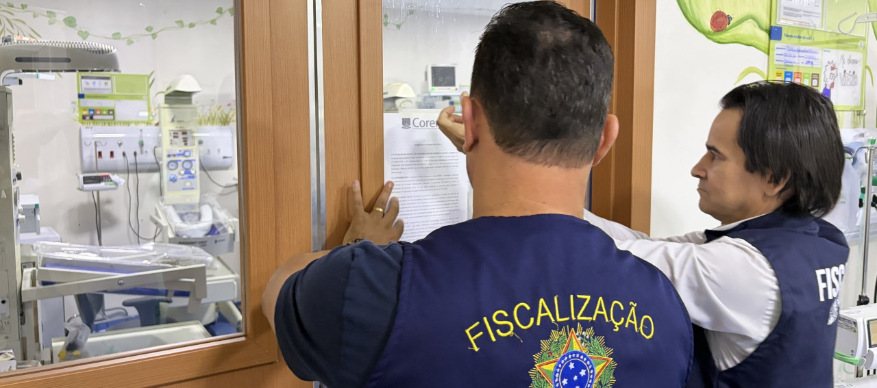 Duas pessoas colando um documento na porta de um estabelecimento