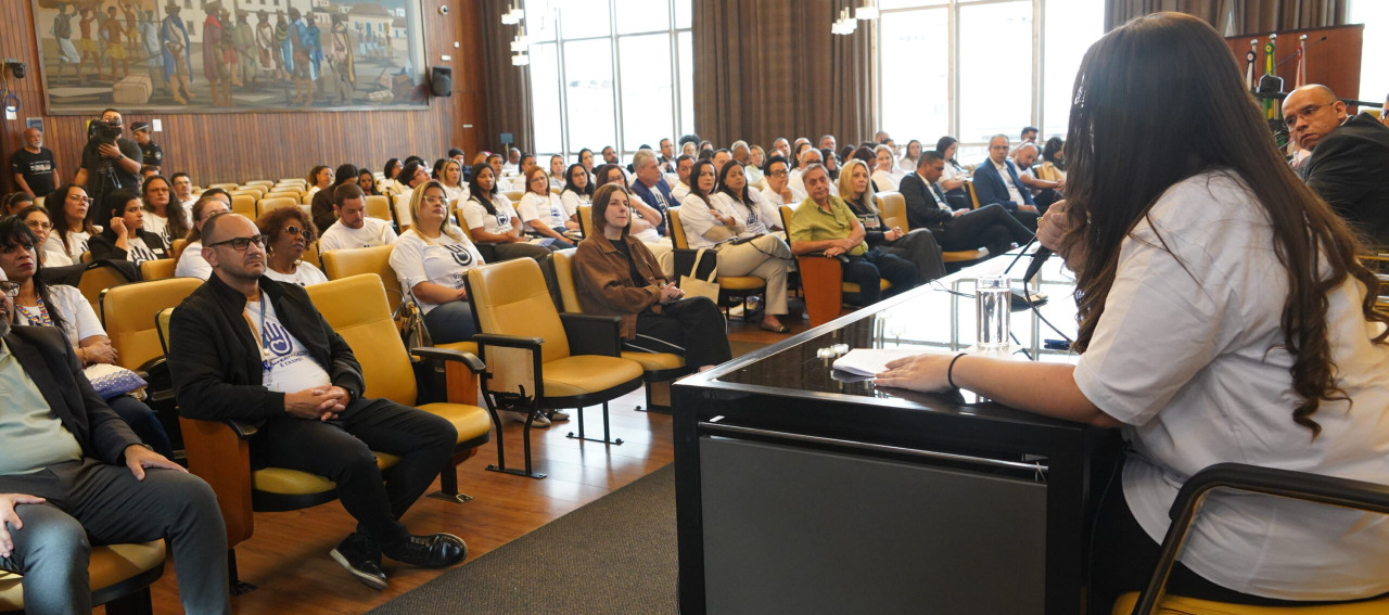 Pessoas sentadas em uma sala acompanhando uma audiência